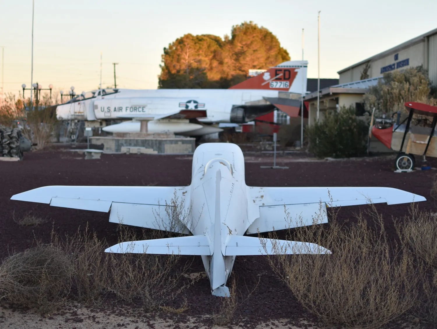 A small custom-made white jet parked on red gravel in front of the museum.